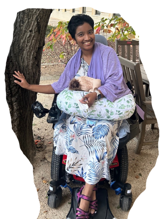 Elena Claire (formerly Harshini Busireddy) smiling outdoors in her wheelchair.